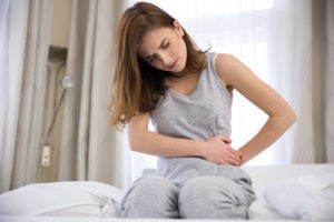 Young woman sitting on the bed with pain