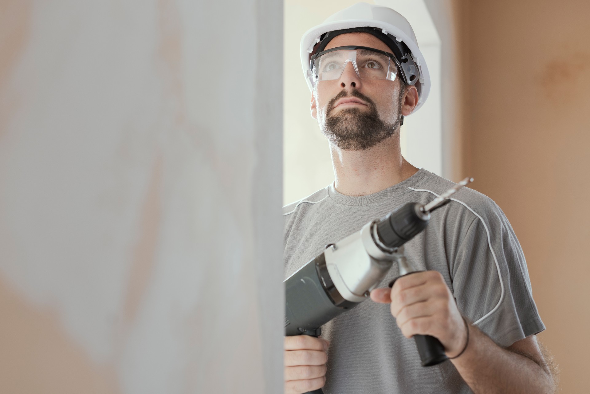 Professional construction worker using a drill, he is wearing a safety helmet and goggles